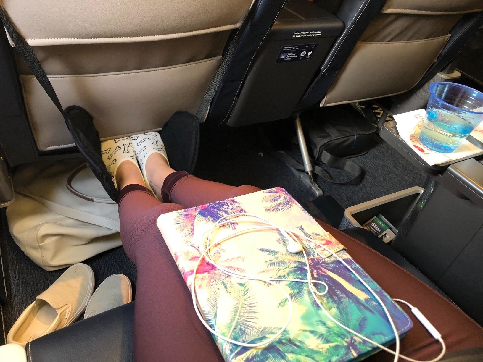 reviewer in an airplane seat with their feet resting on the foot hammock