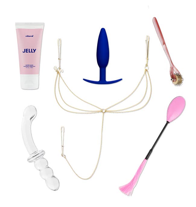 Transparent double-ended dildo, pink crop, goldtone nipple and clitoral clamp, pink bottle of lubricant, blue silicone plug and pink X