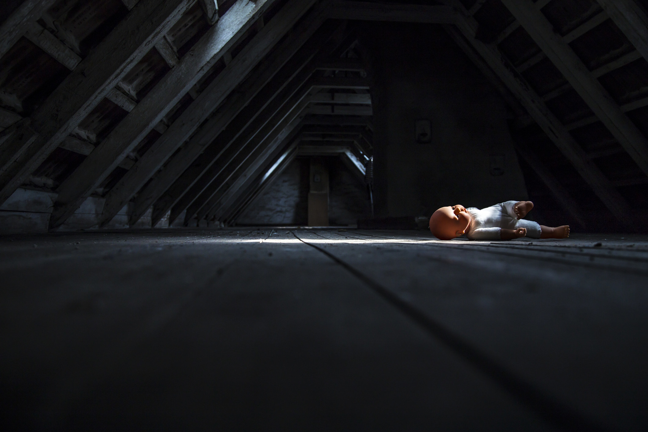 Side view of a dark attic with slanted ceilings with a ray of light on an abandoned baby doll