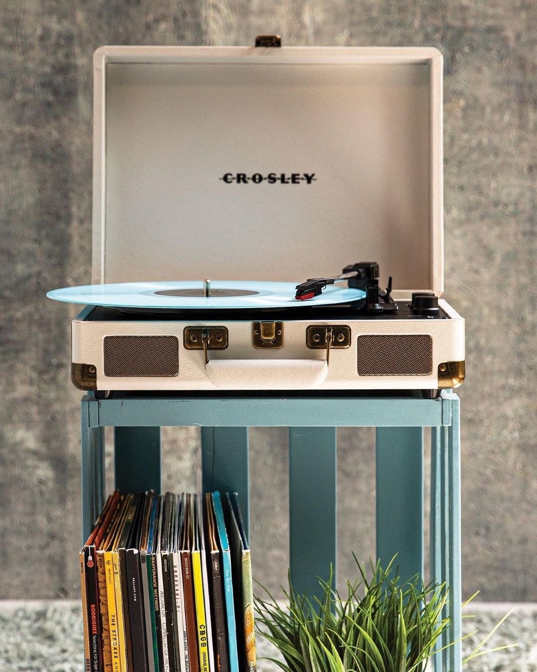 A record player on a small shelf with vinyls stacked below