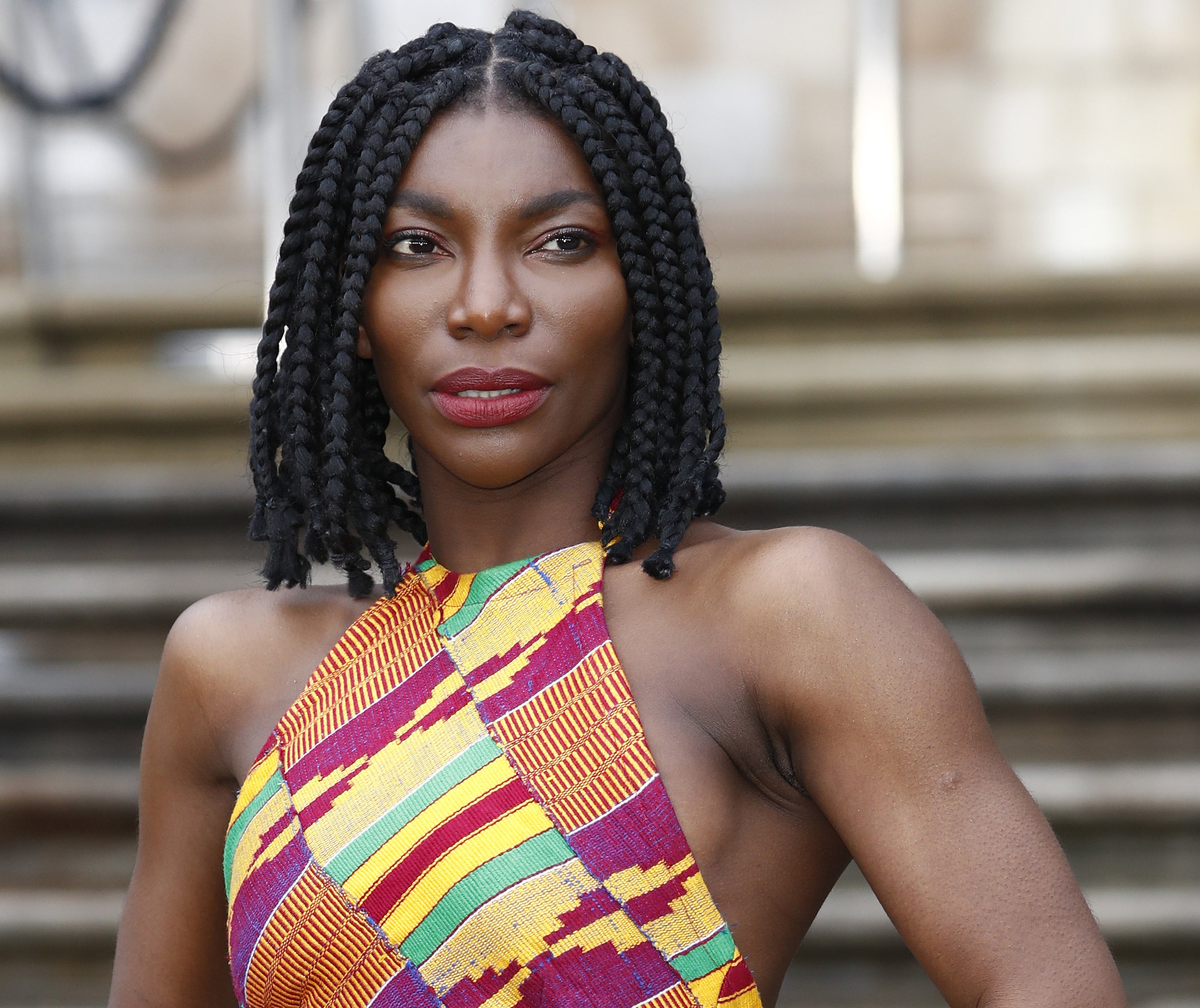 Michaela has shoulder length braided hair while wearing a colorful halter dress