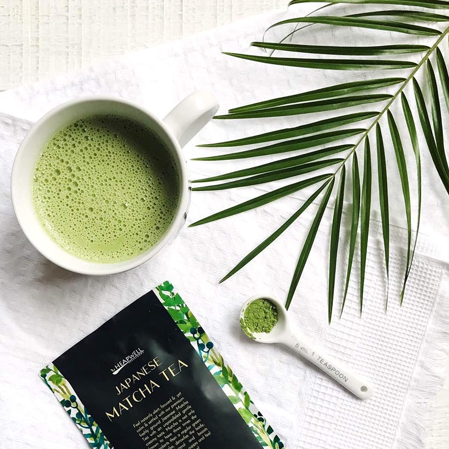 A mug of matcha pictured with a fern and the matcha packet