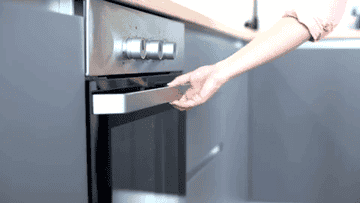 Woman opens oven and begins to take out a tray