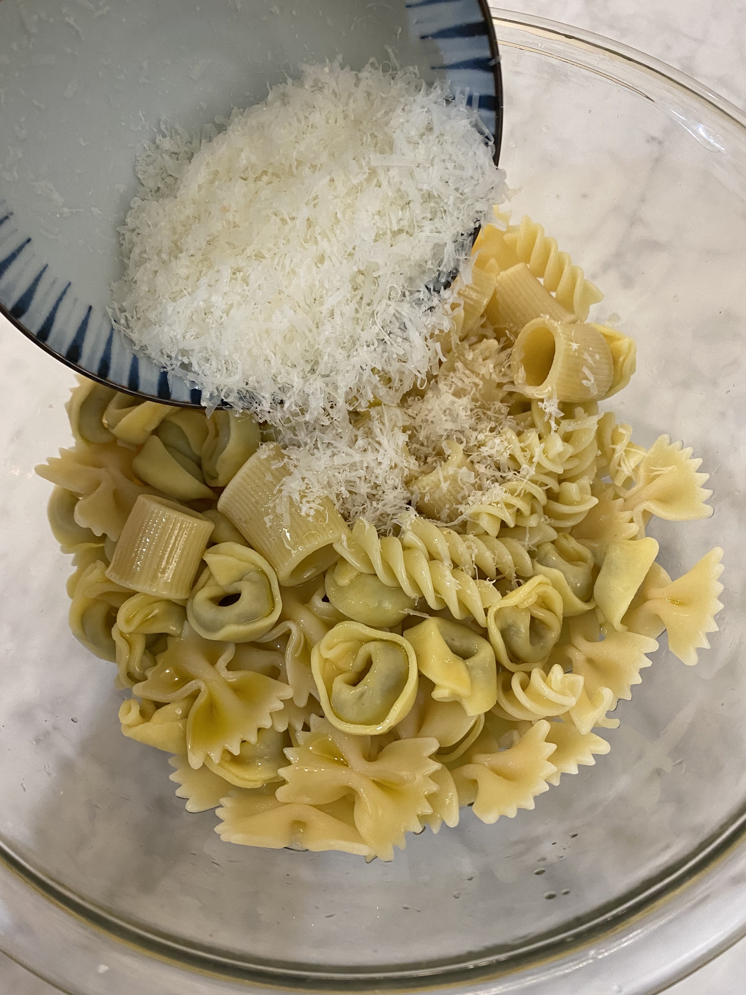 Pouring grated Parmesan cheese onto cooked pasta.