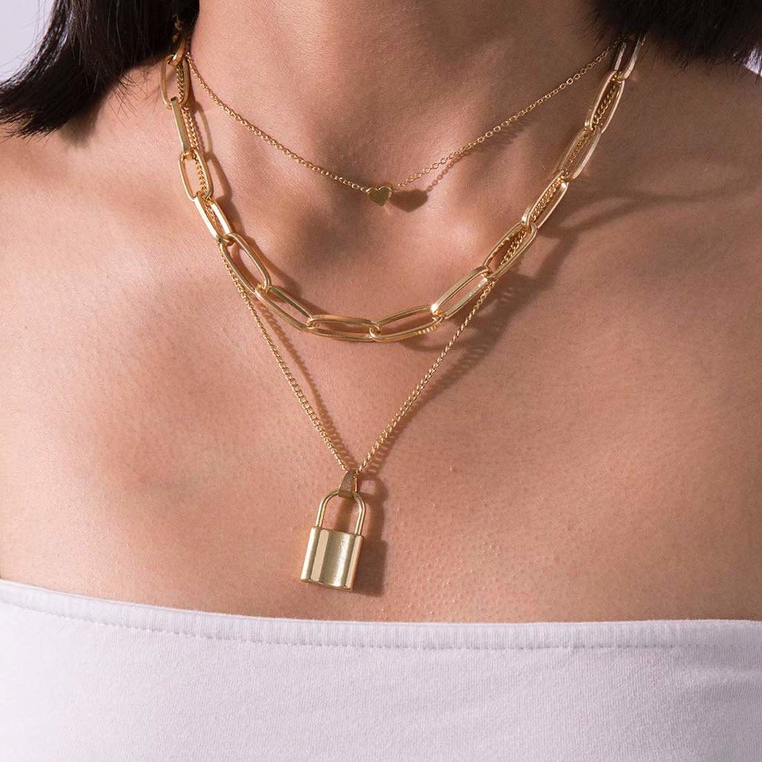 A layered golden necklace consisting of a chain with a lock-shaped charm, a chunky chain, and a delicate chain with a tiny heart in the middle