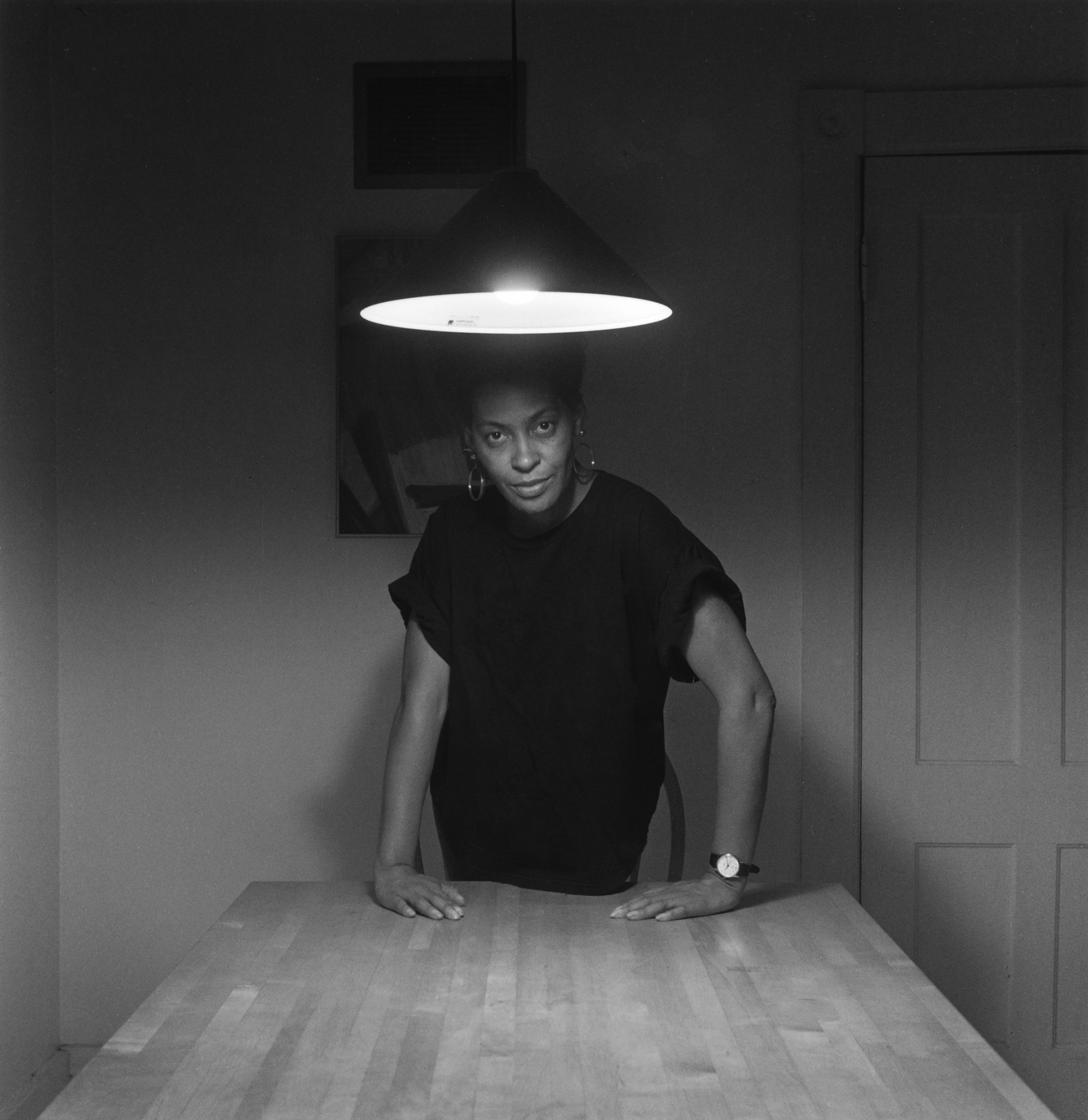 A woman stands under a kitchen light, facing the camera directly 