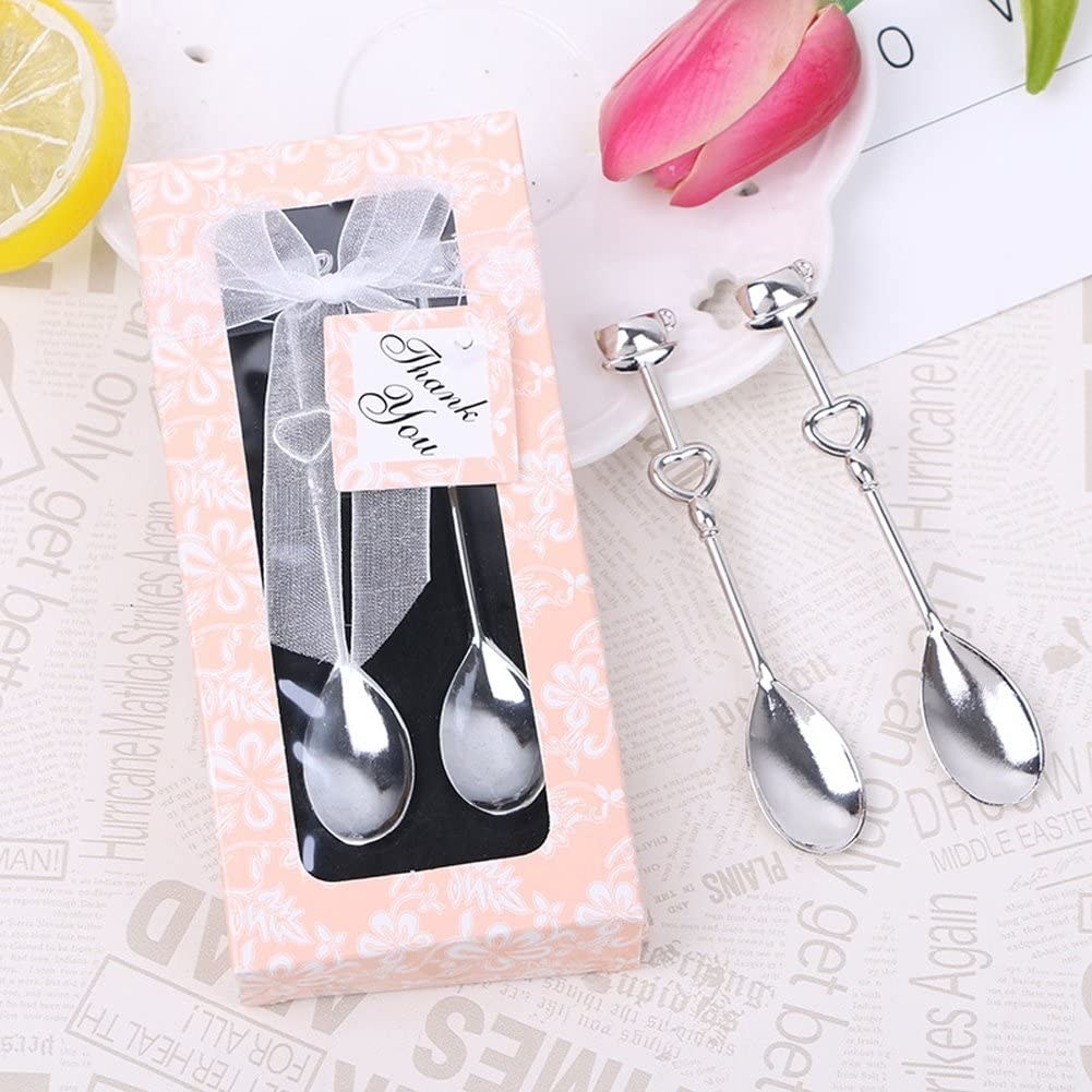 Four teaspoons with a heart shape on the stem, two in a pink gift box and two next to it