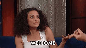 Jenny Slate dancing in her seat saying welcome in a scene from the late show with stephen colbert