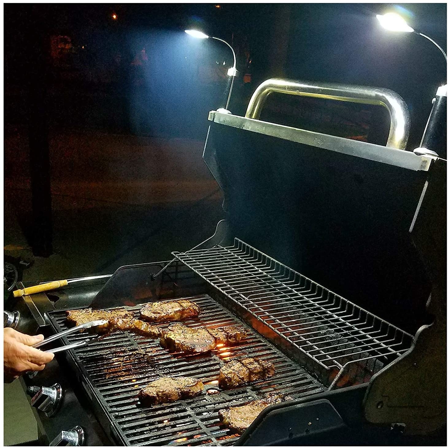 Model grilling meat on a barbecue at night while using the lights, magnetically attached to the grill