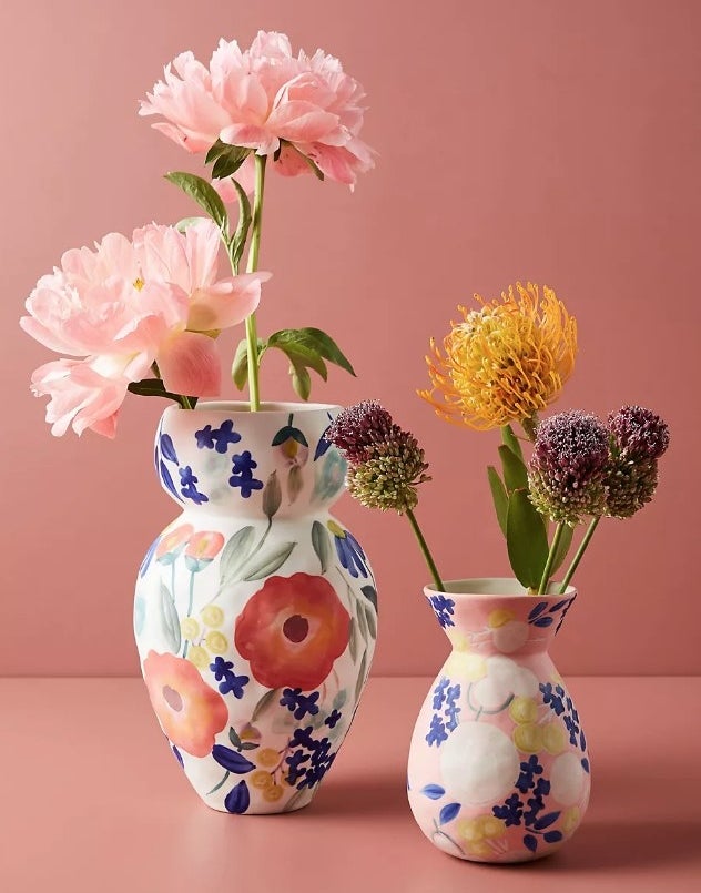 Two handcrafted stoneware vases; one larger in white and one smaller in pink, both painted with floral designs and filled with flowers