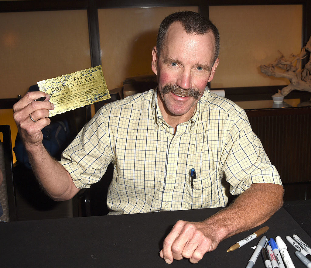 A grown up Peter Ostrum posing with a golden ticket