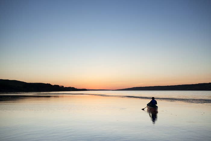 A photo of a person canoeing on a lake during sunset