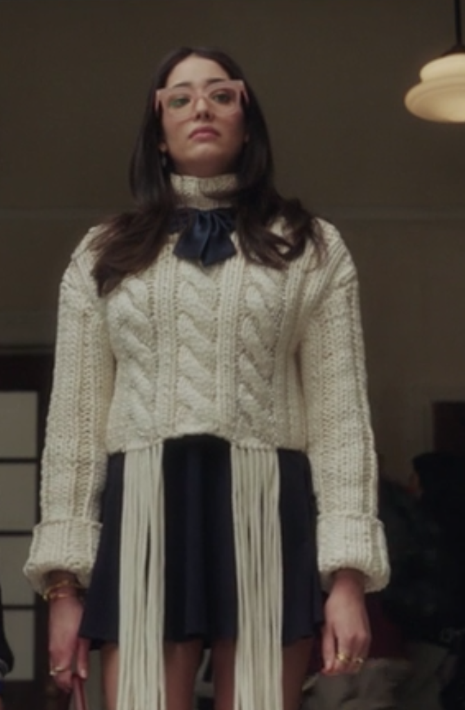 Luna wears a dark, high-waisted ruffle skirt and a knit sweater with fringe on the hem