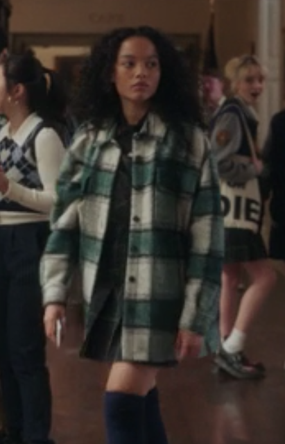 Zoya wears an oversize plaid wool coat over a plaid uniform skirt and knee-length socks