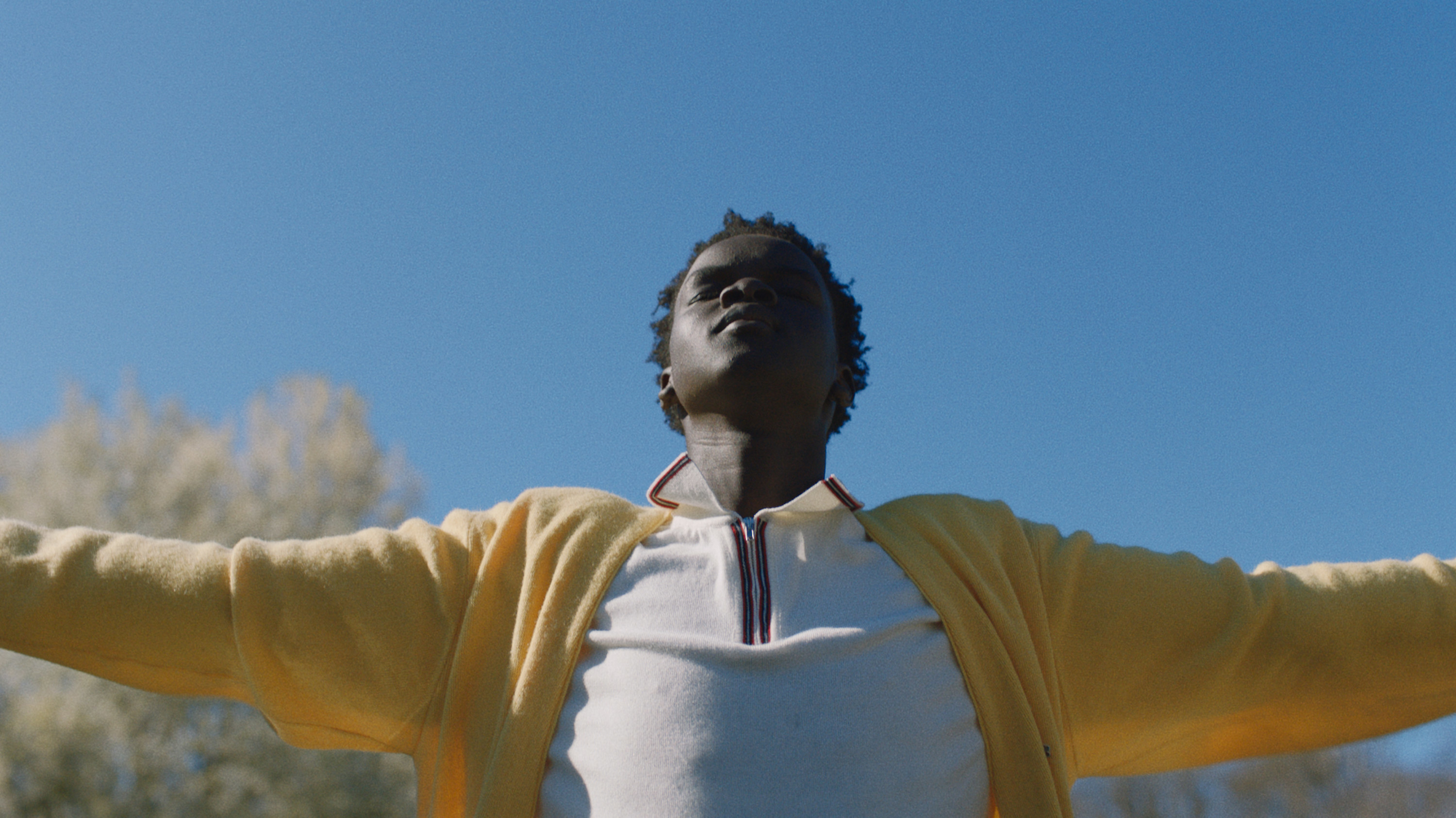 A young man with arms spread wide raises his face to the sun with his eyes closed