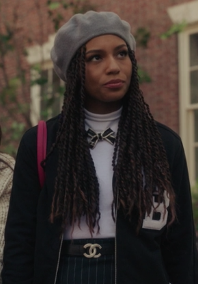 Monet wears a high-waisted pin-striped skirt with a T-shirt tucked into it under a dark letterman jacket and a beret