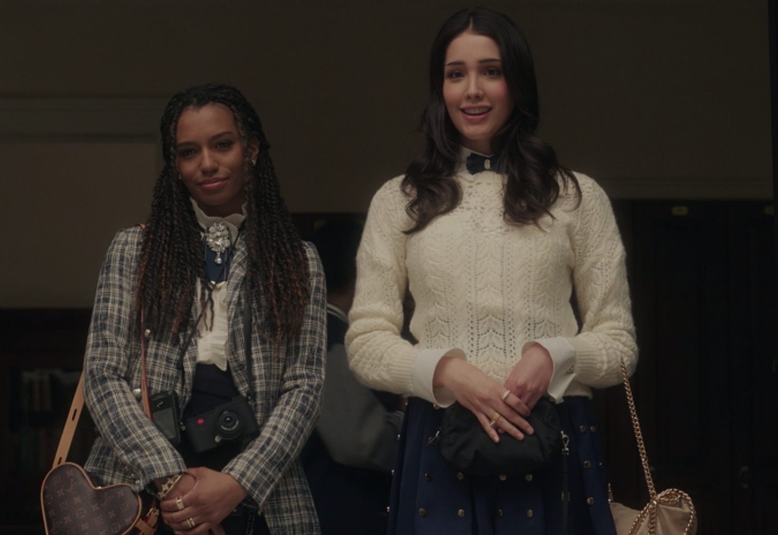 Monet wears a tight-fitting plaid blazer over a top with ruffles on it, and Luna wears a studded high-waisted skirt and a knit sweater