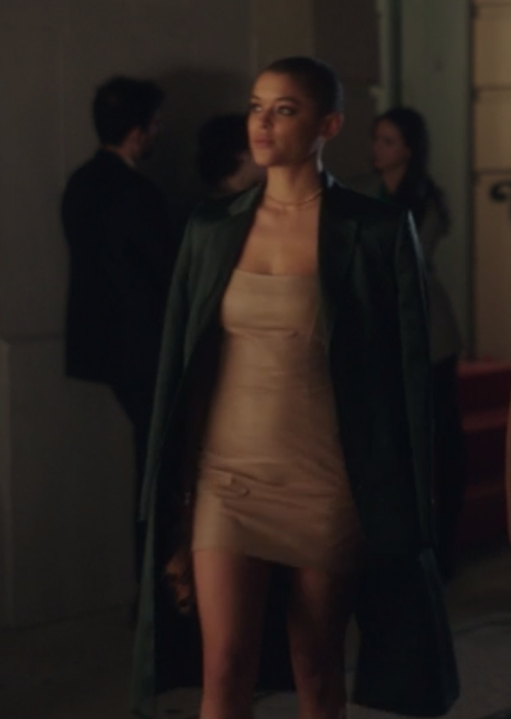 Julien wears a long dark trench coat over a tight-fitting minidress