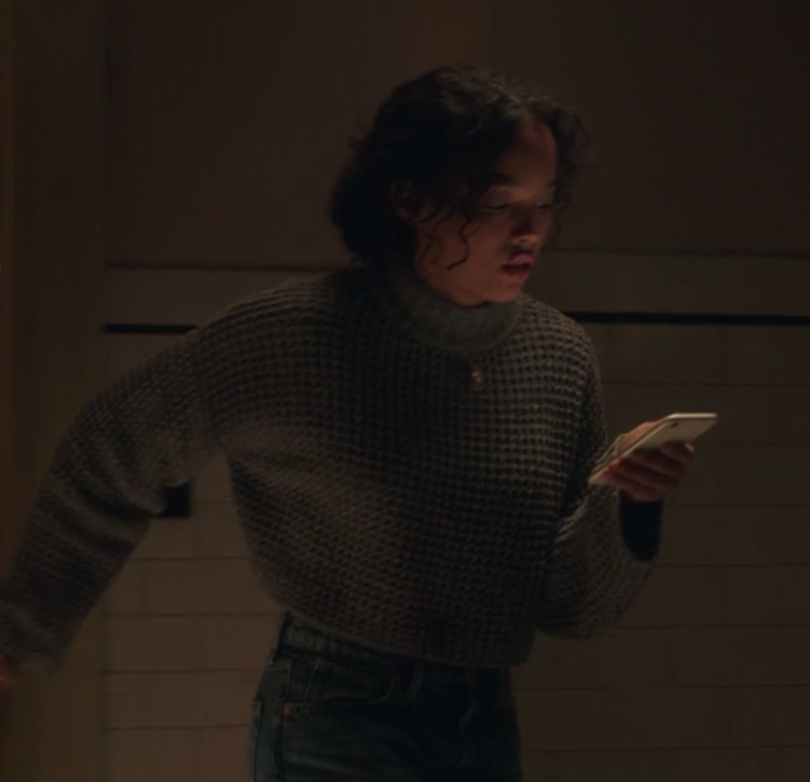 Zoya wears a dark cropped cowl-neck sweater and high-waisted jeans