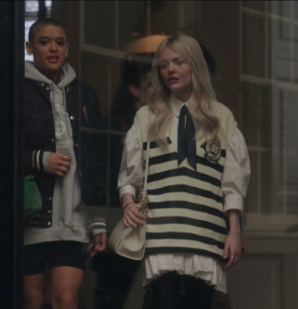 Julien wears biker shorts and an oversize hooded sweatshirt under a letterman jacket. Audrey wears a striped vest over a white lace long-sleeved shirt