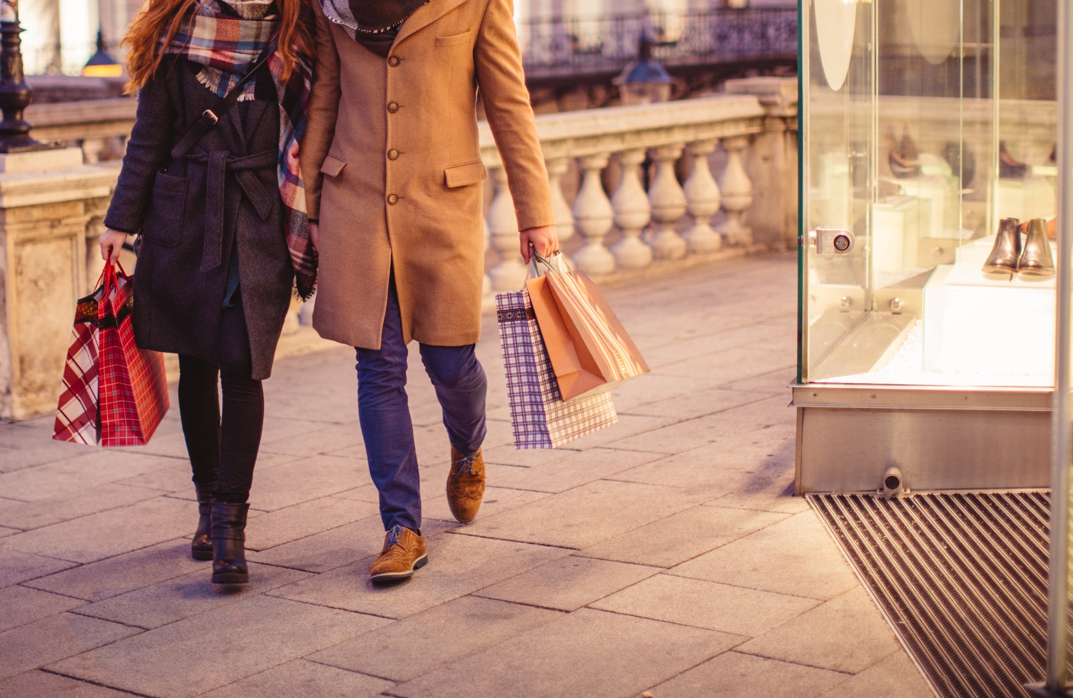 A couple holding shopping bags as they walk past a store