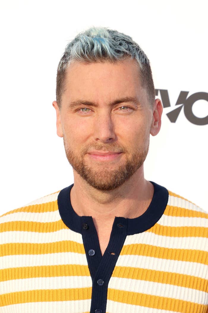 Lance Bass smiles at a red carpet event while wearing a striped sweater