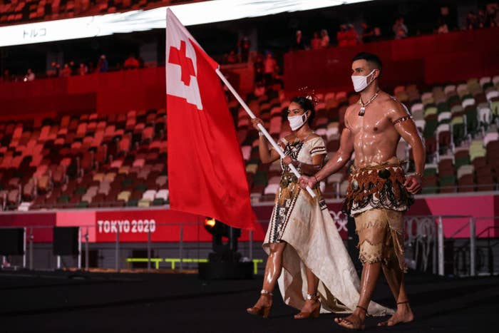 Pita Taufatofua is seen with an oily, muscled chest as he marches through an empty stadium carrying Tonga&#x27;s flag next to his fellow athletes