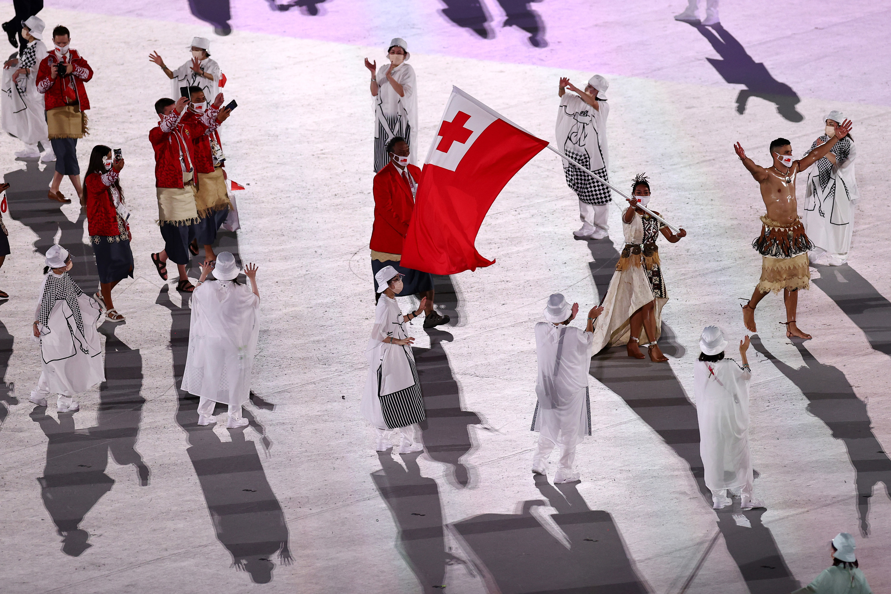 Pita Taufatofua is seen with an oily, muscled chest as he marches through an empty stadium carrying Tonga&#x27;s flag next to his fellow athletes