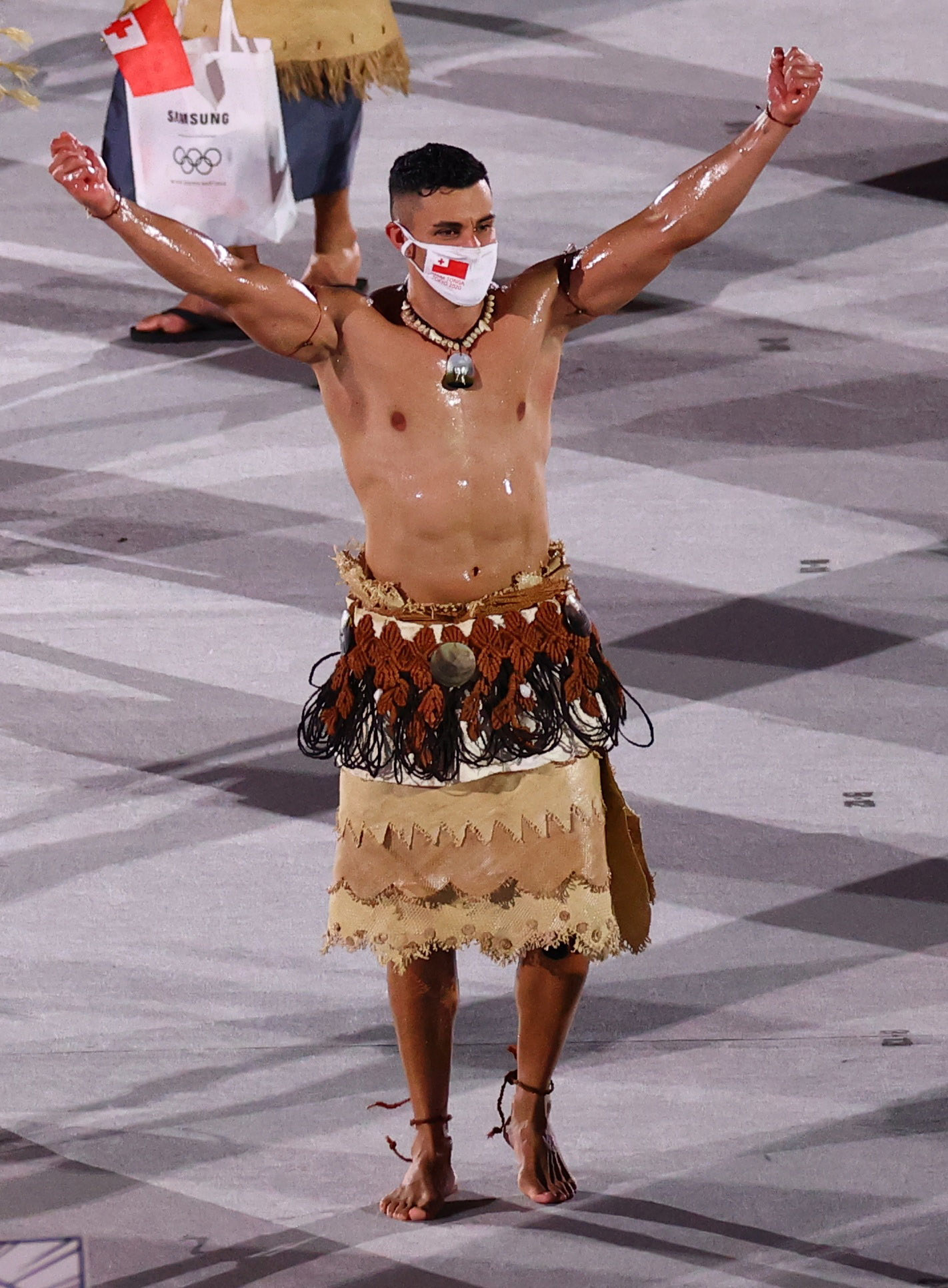 Pita Taufatofua is seen with an oily, muscled chest as he marches through an empty stadium carrying Tonga&#x27;s flag next to his fellow athletes