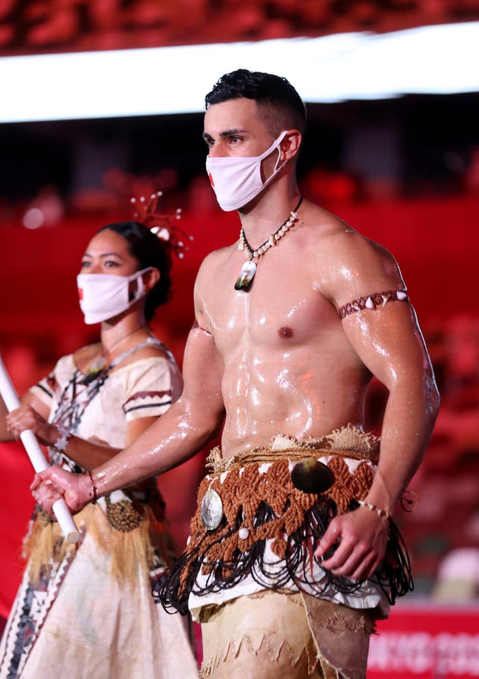 Pita Taufatofua is seen with an oily, muscled chest as he marches through an empty stadium carrying Tonga&#x27;s flag next to his fellow athletes
