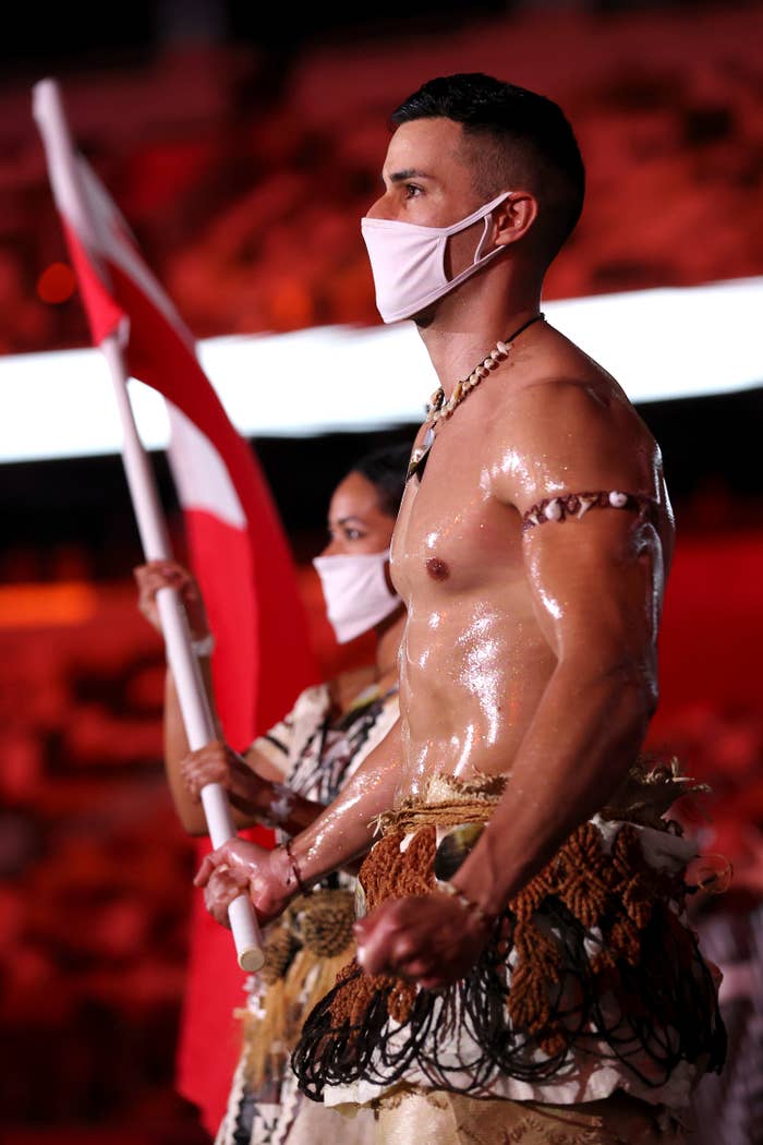 Pita Taufatofua is seen with an oily, muscled chest as he marches through an empty stadium carrying Tonga&#x27;s flag next to his fellow athletes