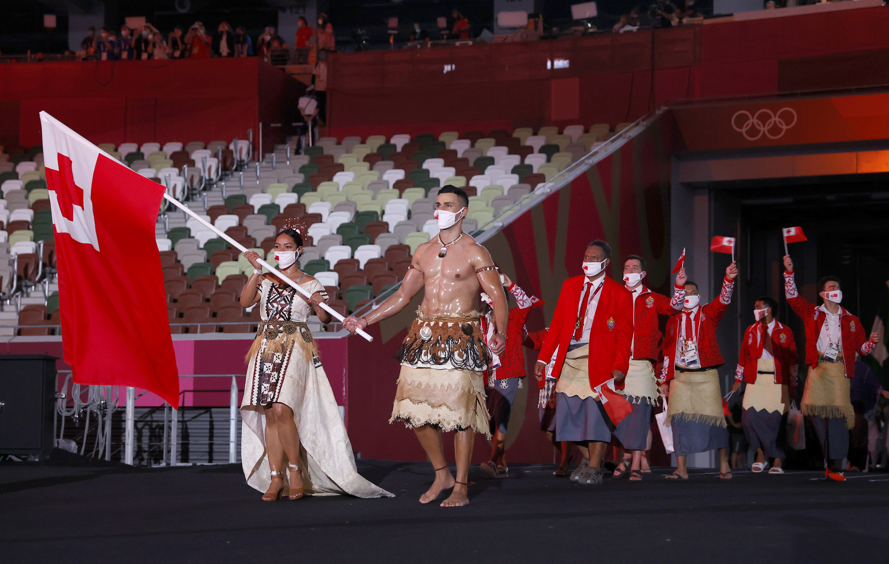 Pita Taufatofua is seen with an oily, muscled chest as he marches through an empty stadium carrying Tonga&#x27;s flag next to his fellow athletes