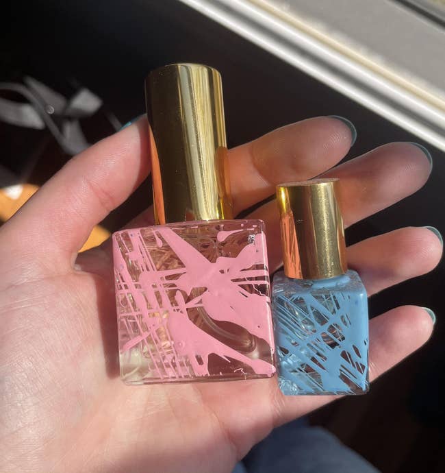 the writer holding cubic perfume bottles with pink and blue paint splatters on them and gold caps