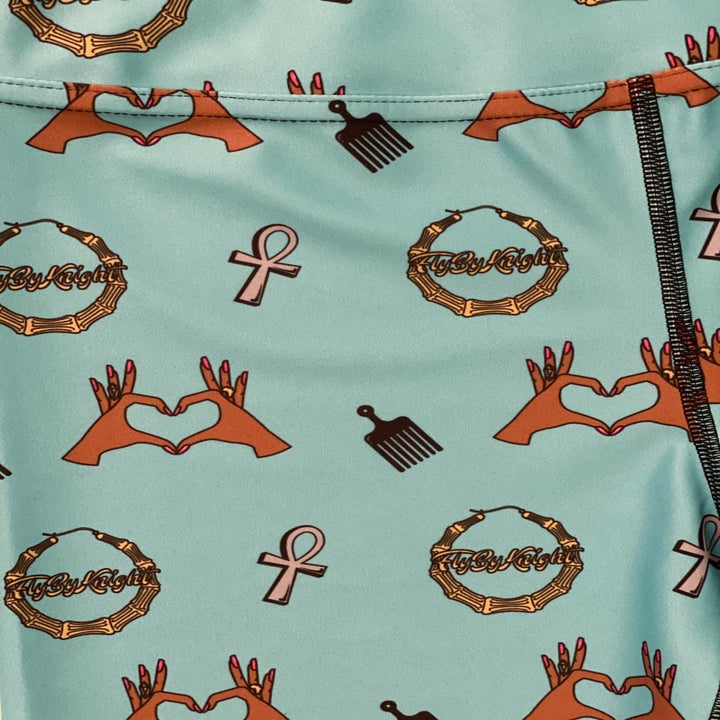 a close up of the print which features and ankh, a pic, a hoop earring, and two hands making a heart shape