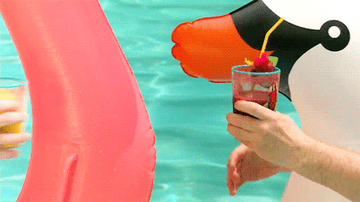 Conan and Andy cheers and take a sip of their drinks while relaxing on swan- and flamingo-shaped floaties in a pool