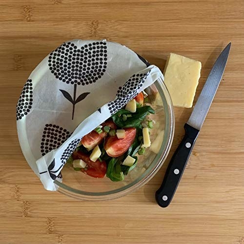 A bowl of freshly cut salad half-covered with the beeswax food wrap and a knife placed on the side
