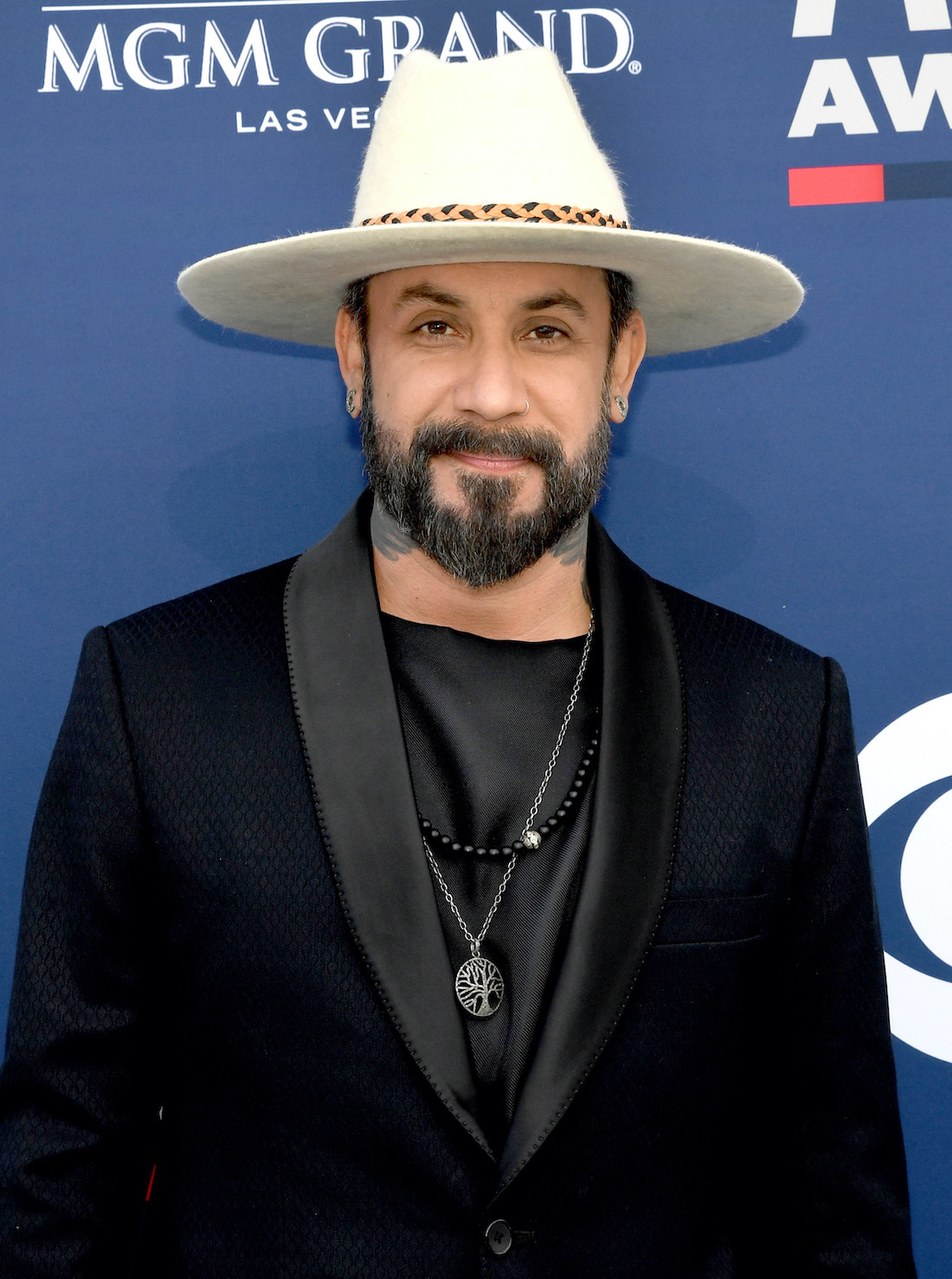 AJ McLean wears a suit, pendant, and brimmed hat at a red carpet event