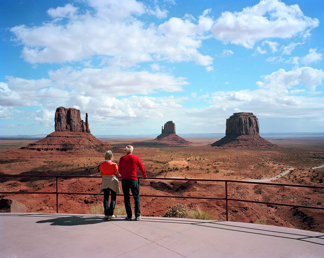 Two people stand at a rail and gaze out at red rock on a sunny day