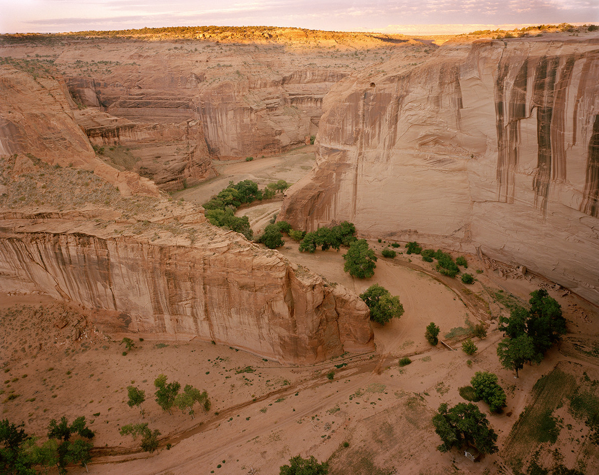 Scene of red rock shows pathways and some green shrubs and trees