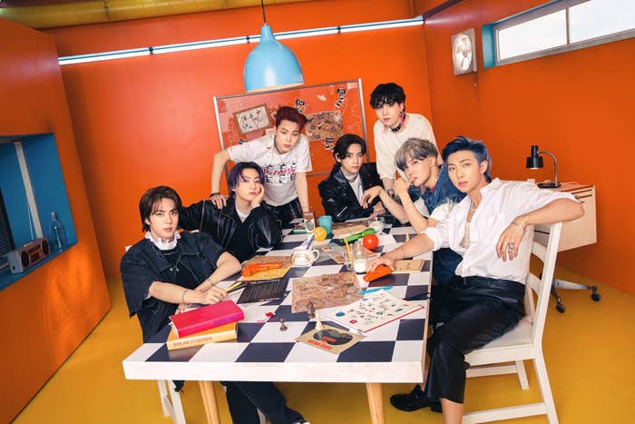 BTS poses while sitting at a table filled with books and games