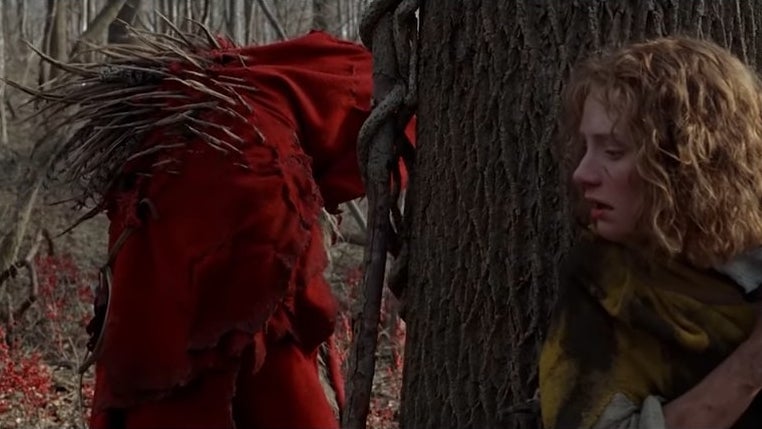 Bryce Dallas Howard hides behind a tree from a creature in a red cloak