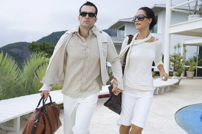 A wealthy couple walk hand-in-hand by a pool