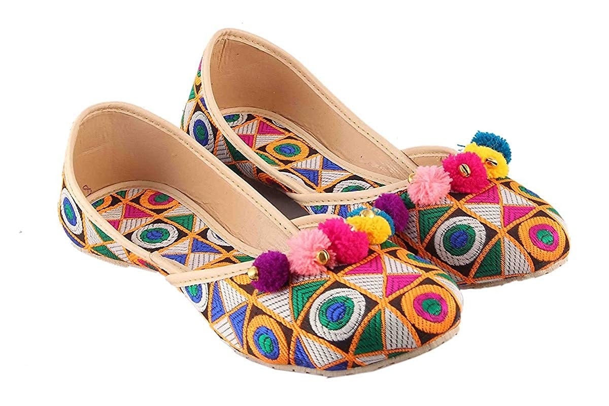 A pair of colourful Jaipuri juttis with a geometric design and colourful pom poms attached to the rim
