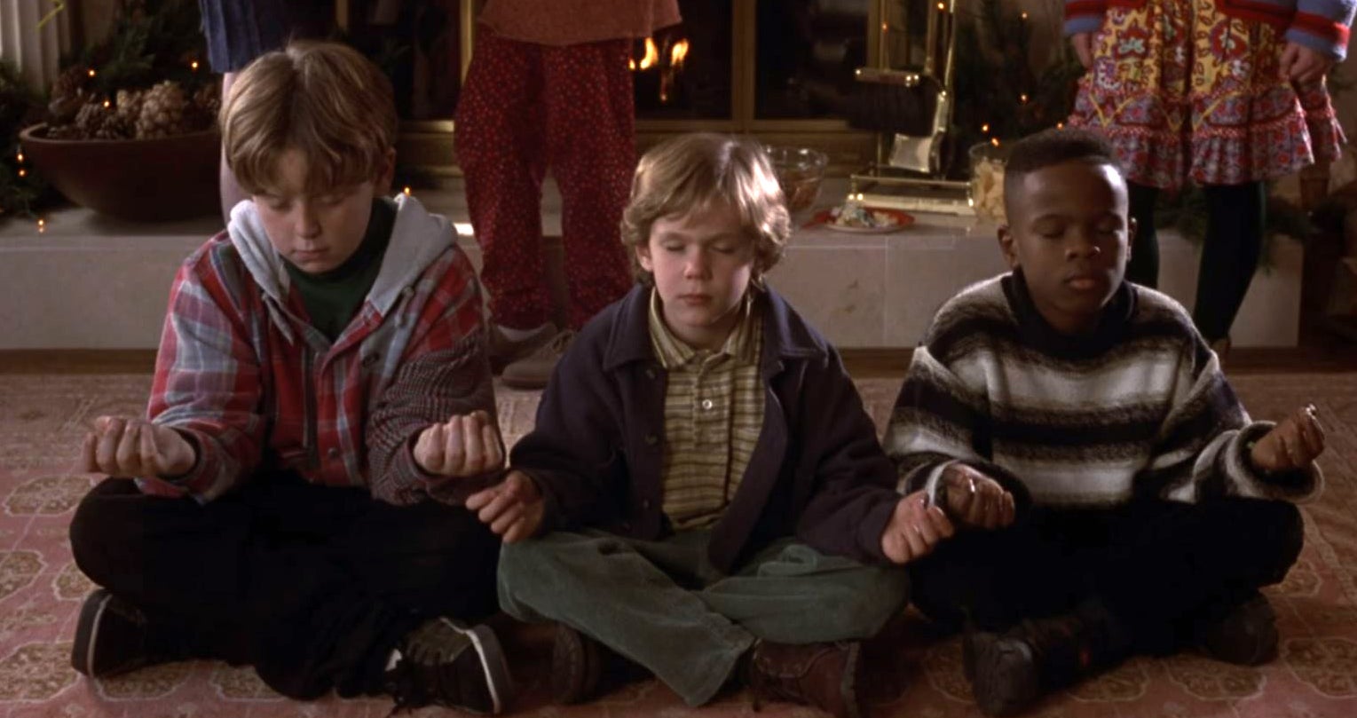 Three kids sit cross-legged on the floor, meditating at a party