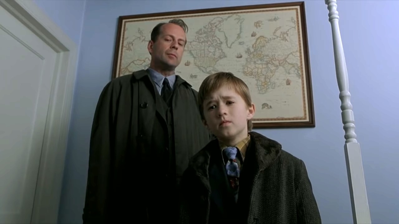 Bruce Willis and Haley Joel Osment look down at something with concern