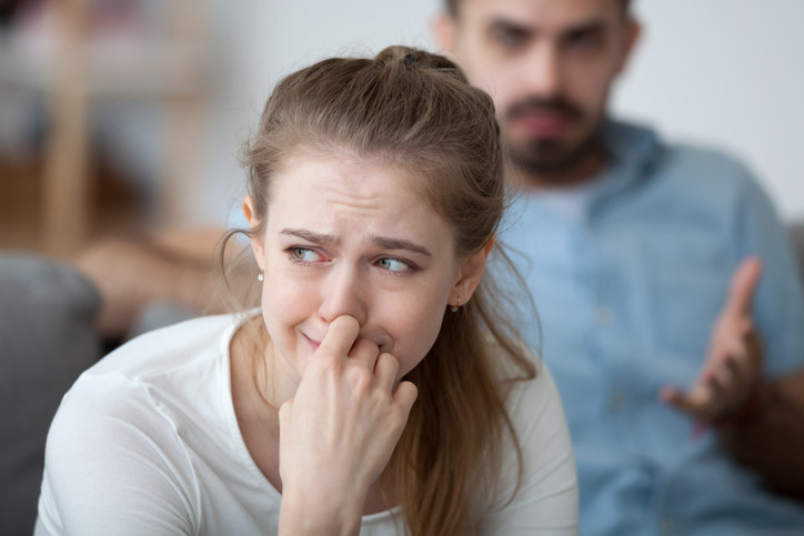 Woman crying while her husband is upset behind her