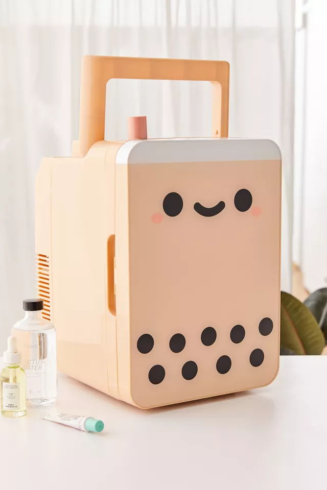 A tiny fridge on a table with beauty products beside it