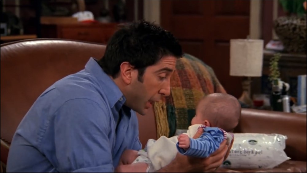 Ross cradles his newborn daughter close to his face as he sits on the couch