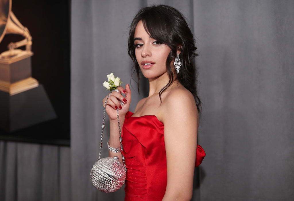 Camila wearing a sleeveless red outfit and a small sparkly ball handbag
