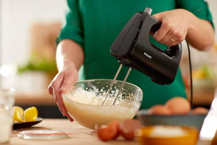 A person blending batter in a bowl with the hand mixer